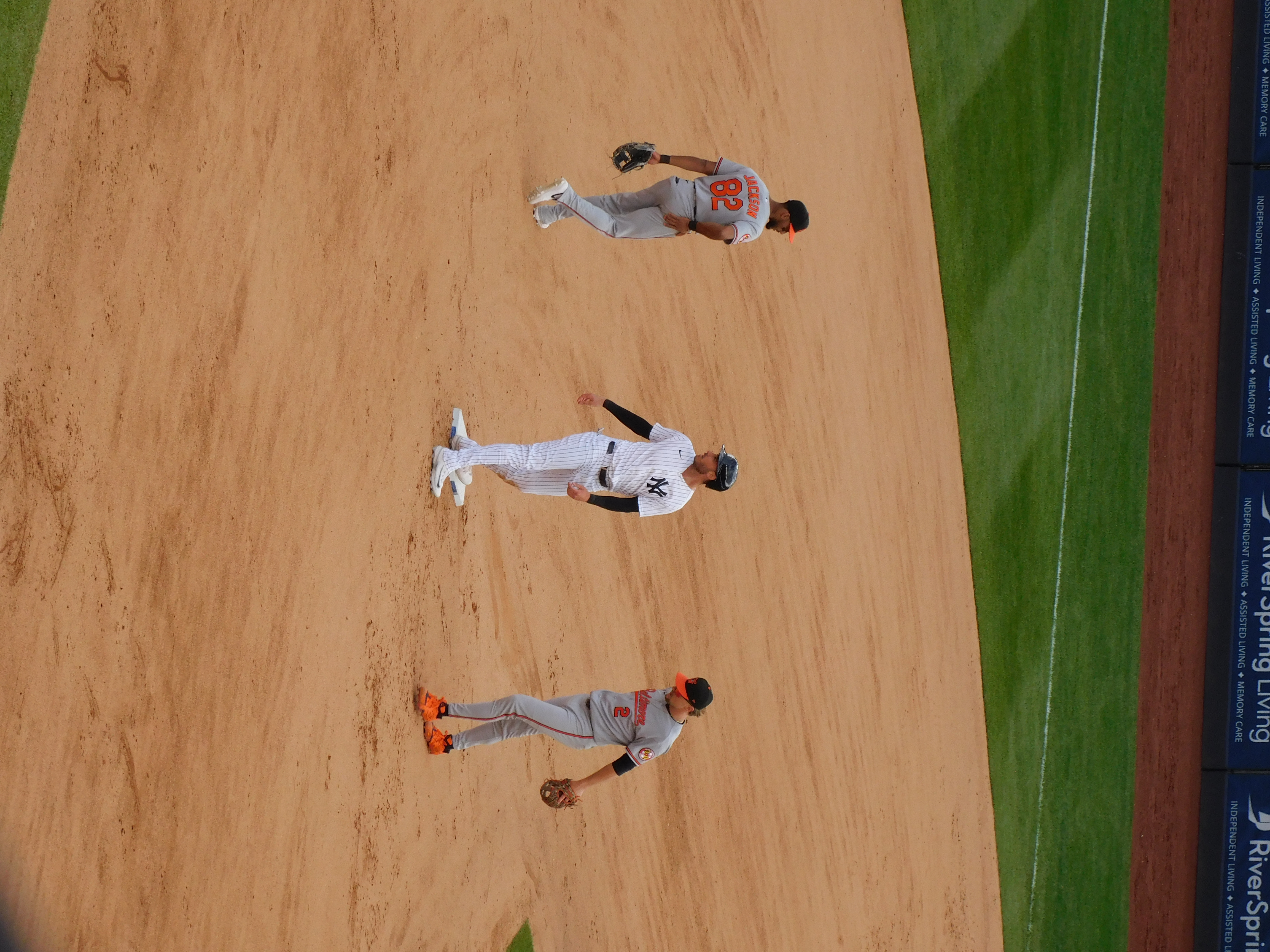 Three baseball players standing in the infield during a game. The player in the middle is Yankees outfielder Cody Bellinger, who is standing on 2nd base after hitting a double. The players on his left and right are Orioles players returning to their defensive positions.